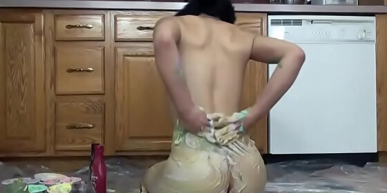 a gorgeous chick with long hair coats her slender body and beautiful tits with colored paints in the kitchen